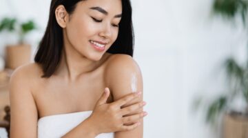 smiling asian girl applying body lotion on her sho Z8X6Y68 2500x